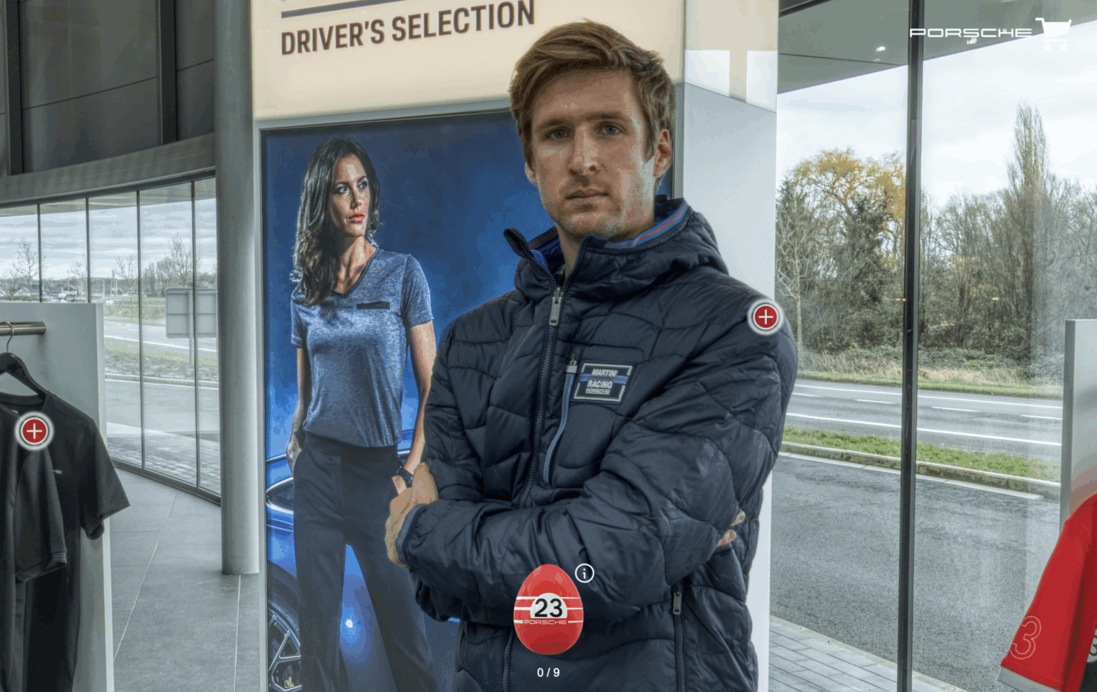 A man in a dark Porsche jacket stands confidently with arms crossed in the Porsche Driver’s Selection boutique, surrounded by branded merchandise and apparel.